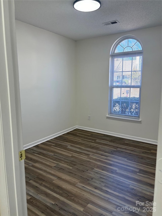 spare room with a textured ceiling and dark hardwood / wood-style flooring