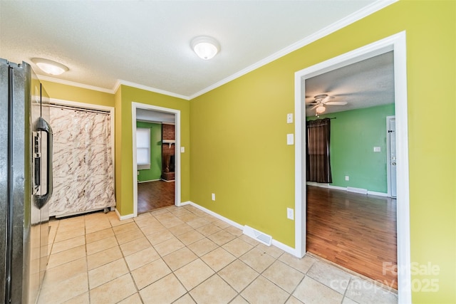 unfurnished bedroom featuring crown molding, black refrigerator, light tile patterned floors, and a textured ceiling