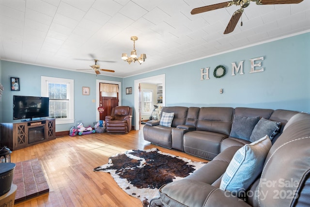 living room with wood-type flooring, ceiling fan with notable chandelier, and ornamental molding