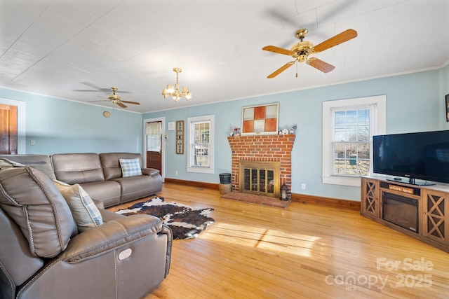 living room with ceiling fan with notable chandelier, a brick fireplace, light hardwood / wood-style flooring, and crown molding