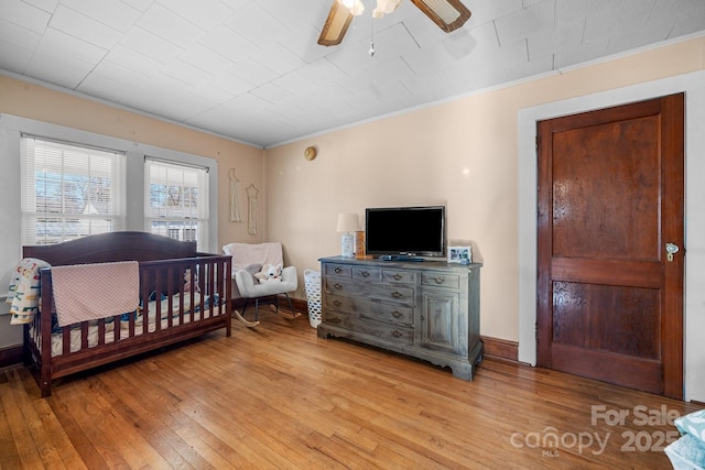 bedroom with light hardwood / wood-style flooring, a nursery area, ceiling fan, and ornamental molding