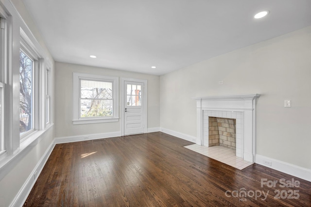 unfurnished living room with hardwood / wood-style flooring, a tile fireplace, and a healthy amount of sunlight