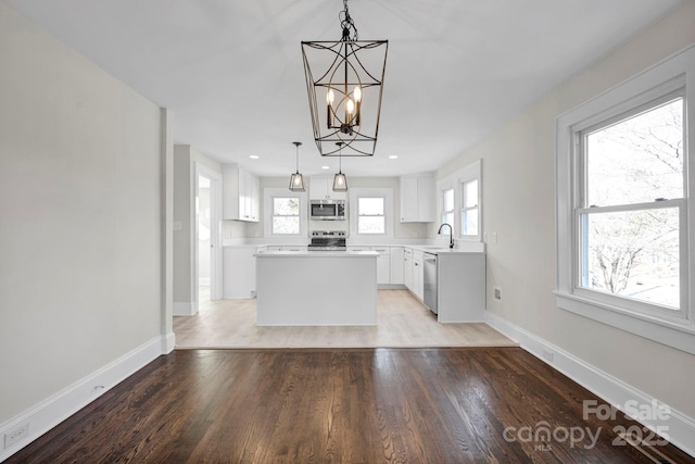 kitchen with white cabinets, appliances with stainless steel finishes, a kitchen island, decorative light fixtures, and light wood-type flooring