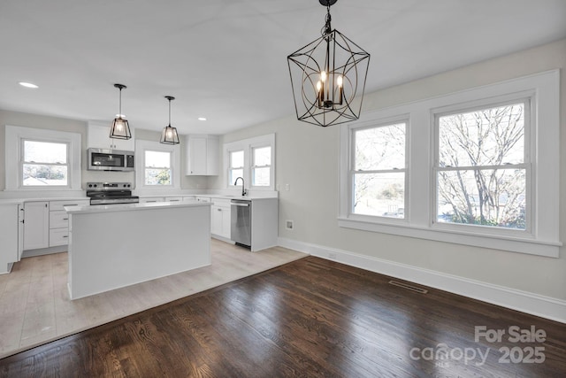 kitchen with decorative light fixtures, white cabinetry, stainless steel appliances, and a kitchen island