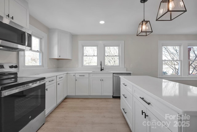 kitchen with sink, white cabinetry, hanging light fixtures, and appliances with stainless steel finishes