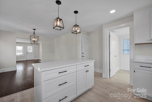 kitchen with a kitchen island, light wood-type flooring, white cabinetry, and decorative light fixtures