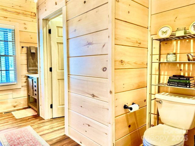 bathroom featuring hardwood / wood-style flooring, wooden walls, and toilet