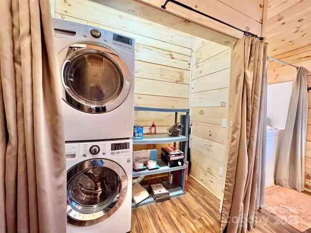 clothes washing area featuring hardwood / wood-style floors, wooden walls, and stacked washing maching and dryer