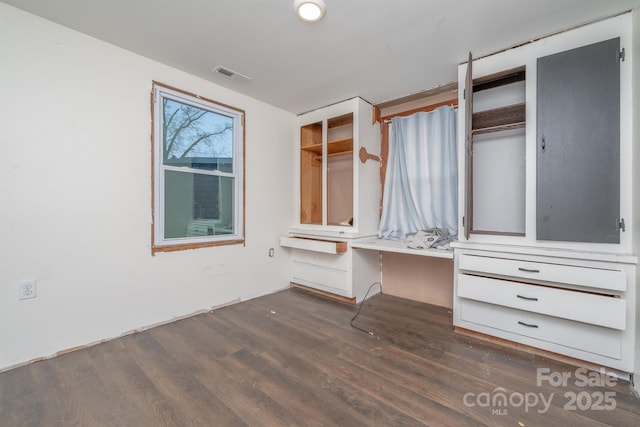 unfurnished bedroom featuring built in desk and dark wood-type flooring