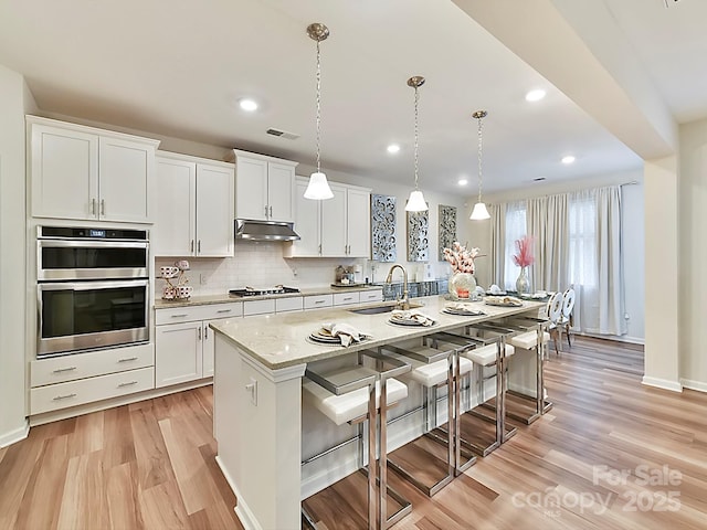 kitchen featuring an island with sink, white cabinetry, sink, and decorative light fixtures