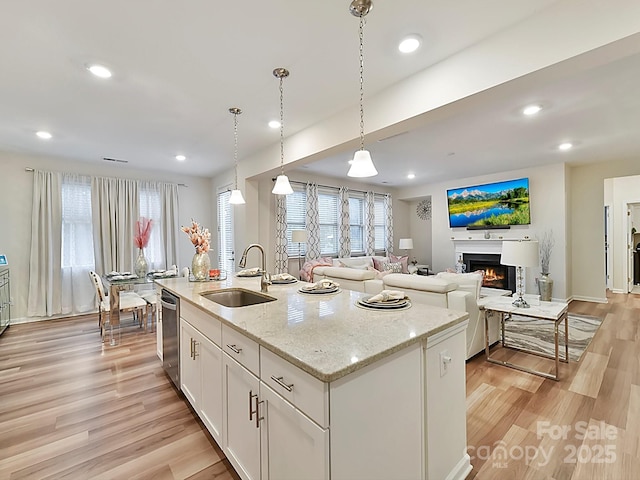 kitchen with dishwasher, white cabinets, decorative light fixtures, sink, and a kitchen island with sink