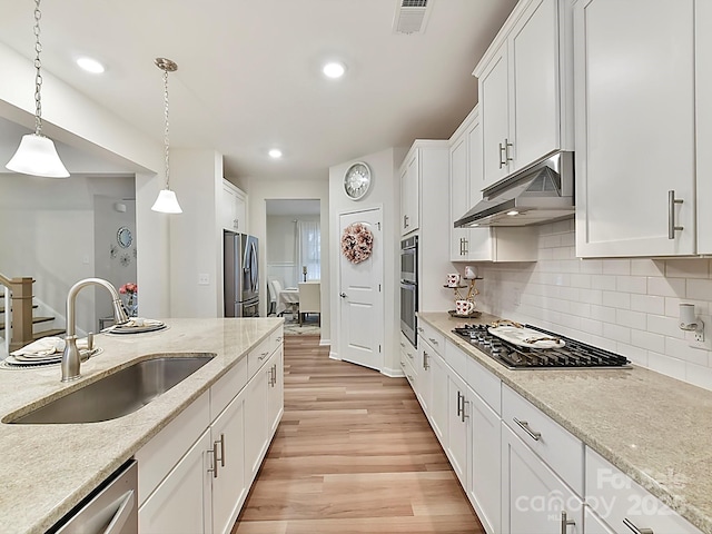 kitchen with appliances with stainless steel finishes, sink, light wood-type flooring, white cabinetry, and hanging light fixtures