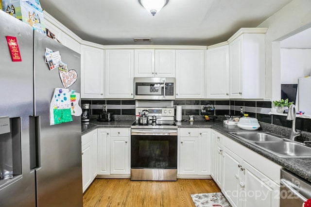 kitchen with sink, appliances with stainless steel finishes, tasteful backsplash, white cabinets, and light wood-type flooring