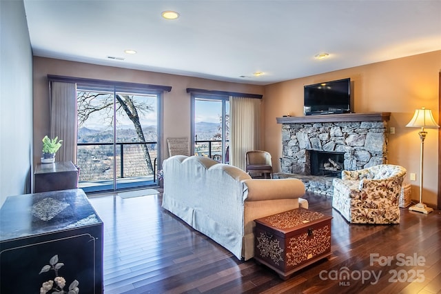 living area with a stone fireplace, dark wood finished floors, visible vents, and recessed lighting