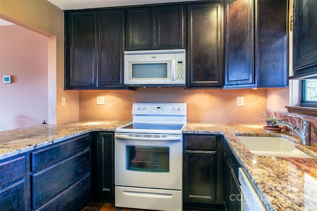 kitchen featuring light stone counters, white appliances, a sink, and dark brown cabinetry