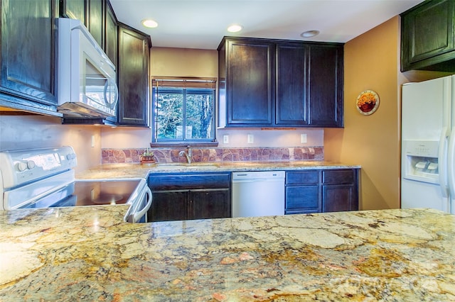 kitchen featuring white appliances, light stone counters, a sink, and recessed lighting