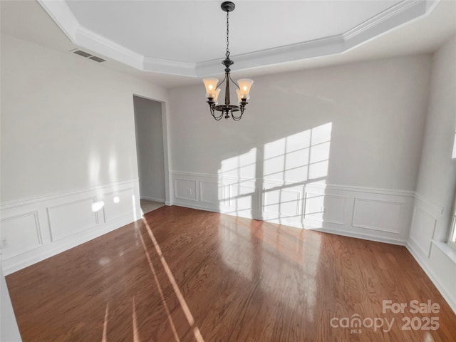 empty room featuring hardwood / wood-style flooring, a notable chandelier, and a raised ceiling