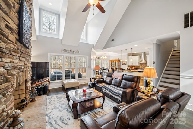 living room with plenty of natural light, a towering ceiling, ceiling fan with notable chandelier, and light wood-type flooring