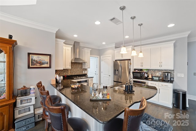 kitchen featuring appliances with stainless steel finishes, white cabinetry, hanging light fixtures, a kitchen bar, and wall chimney exhaust hood