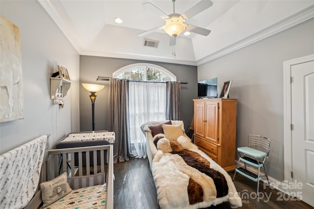 bedroom with ceiling fan, a nursery area, a tray ceiling, ornamental molding, and dark hardwood / wood-style flooring