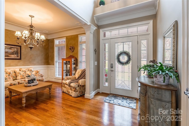 foyer entrance with ornate columns, ornamental molding, a wealth of natural light, and light hardwood / wood-style floors