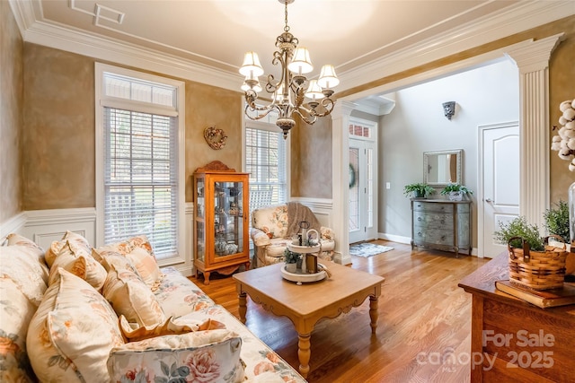 living room with crown molding, ornate columns, a chandelier, and light wood-type flooring