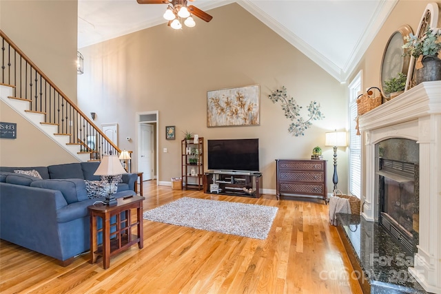 living room featuring crown molding, a premium fireplace, ceiling fan, hardwood / wood-style floors, and a towering ceiling