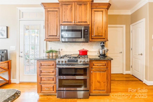 kitchen with dark stone countertops, light wood-type flooring, ornamental molding, and appliances with stainless steel finishes