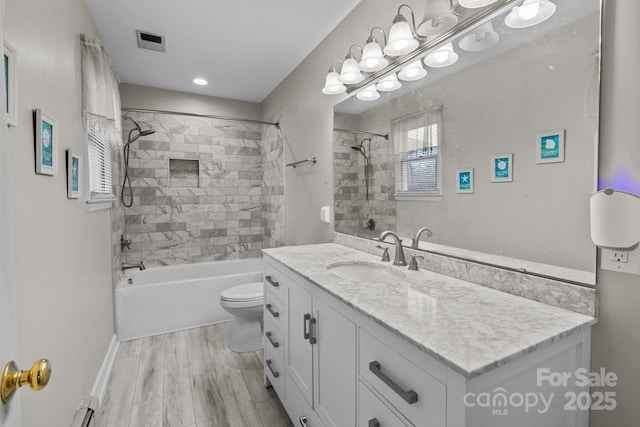 full bathroom featuring hardwood / wood-style floors, vanity, a baseboard heating unit, tiled shower / bath combo, and toilet