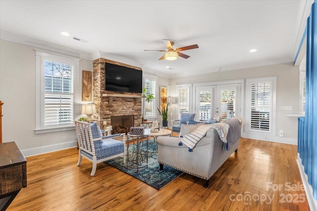 living room with light hardwood / wood-style flooring, ceiling fan, a fireplace, ornamental molding, and french doors