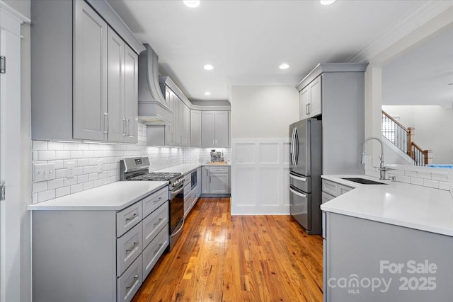 kitchen featuring appliances with stainless steel finishes, sink, gray cabinetry, custom exhaust hood, and light wood-type flooring