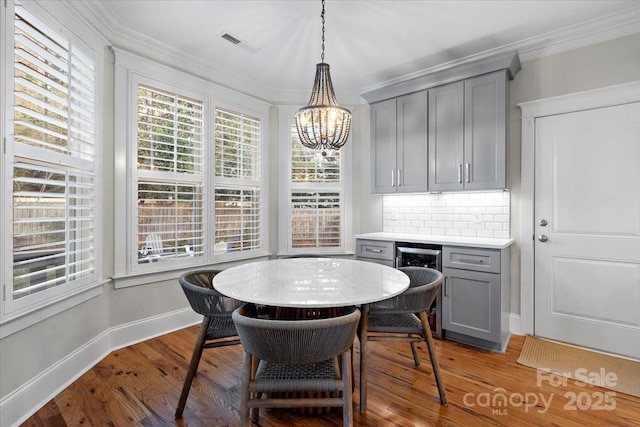 dining room featuring ornamental molding, beverage cooler, light hardwood / wood-style flooring, and a notable chandelier