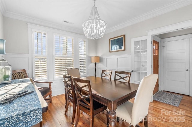 dining space with an inviting chandelier, ornamental molding, and light hardwood / wood-style flooring