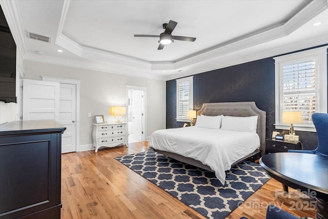 bedroom with light wood-type flooring, ornamental molding, a tray ceiling, ceiling fan, and multiple windows