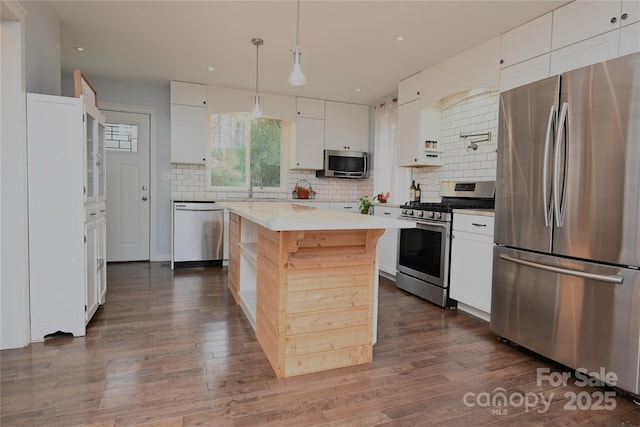 kitchen featuring appliances with stainless steel finishes, tasteful backsplash, white cabinets, hanging light fixtures, and a center island