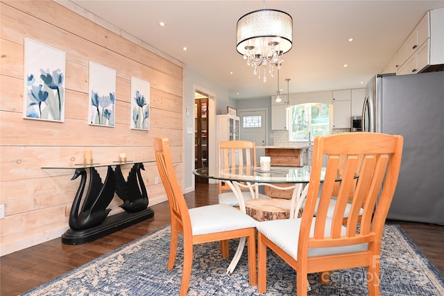 dining space featuring dark wood-type flooring, wooden walls, and a chandelier