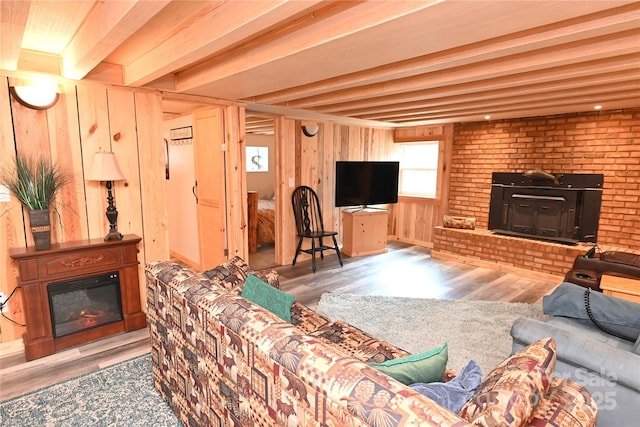 living room featuring wood-type flooring, a fireplace, wooden walls, and beamed ceiling