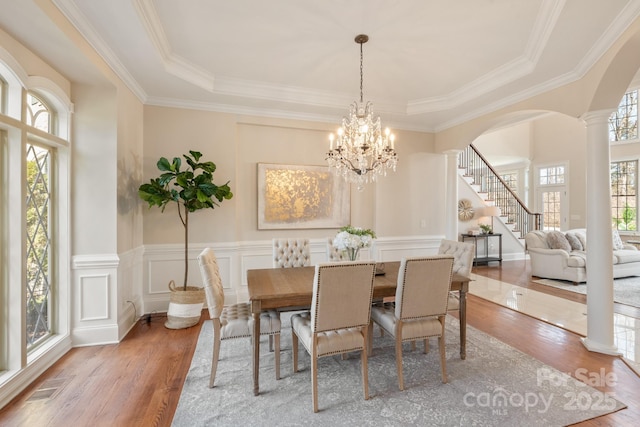 dining area featuring an inviting chandelier, crown molding, wood-type flooring, a raised ceiling, and decorative columns