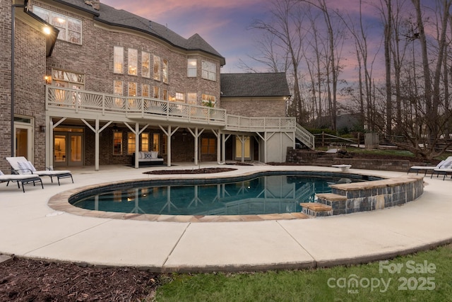 pool at dusk with a patio, a diving board, and a wooden deck