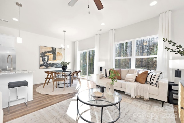 living room with ceiling fan with notable chandelier and light hardwood / wood-style flooring