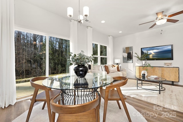 dining space featuring ceiling fan with notable chandelier and wood-type flooring