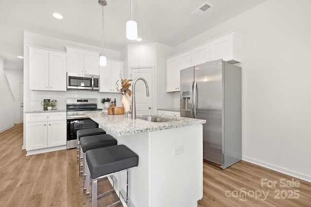 kitchen featuring stainless steel appliances, white cabinetry, sink, and pendant lighting