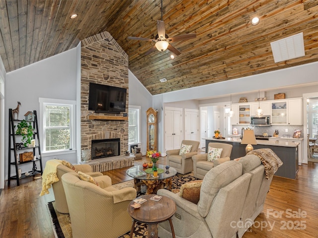 living room with a stone fireplace, high vaulted ceiling, ceiling fan, wood ceiling, and light hardwood / wood-style flooring