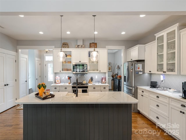 kitchen with hanging light fixtures, an island with sink, appliances with stainless steel finishes, and light stone counters