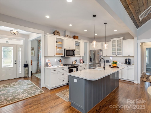 kitchen with stainless steel appliances, white cabinetry, a kitchen island with sink, and pendant lighting