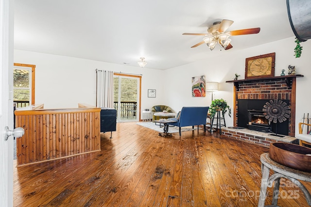 living room featuring wood-type flooring, a brick fireplace, a healthy amount of sunlight, and ceiling fan