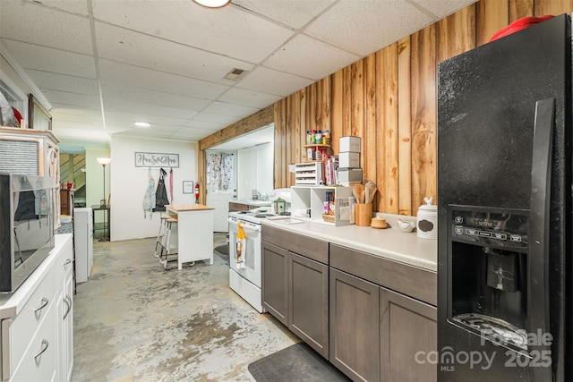 kitchen with black fridge, a paneled ceiling, white range with electric stovetop, and wood walls