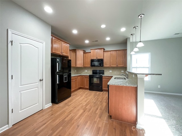 kitchen featuring sink, kitchen peninsula, pendant lighting, light stone countertops, and black appliances