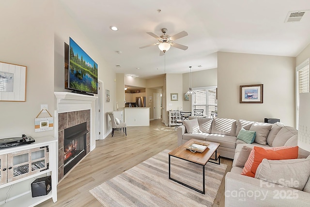 living room with a tiled fireplace, ceiling fan, and light wood-type flooring