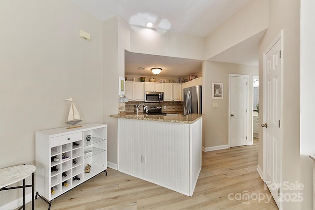 kitchen featuring white cabinetry, light stone counters, appliances with stainless steel finishes, kitchen peninsula, and light hardwood / wood-style floors